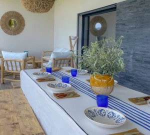 La table à manger extérieure sur le balcon de la villa, dressée avec assiettes et couverts.