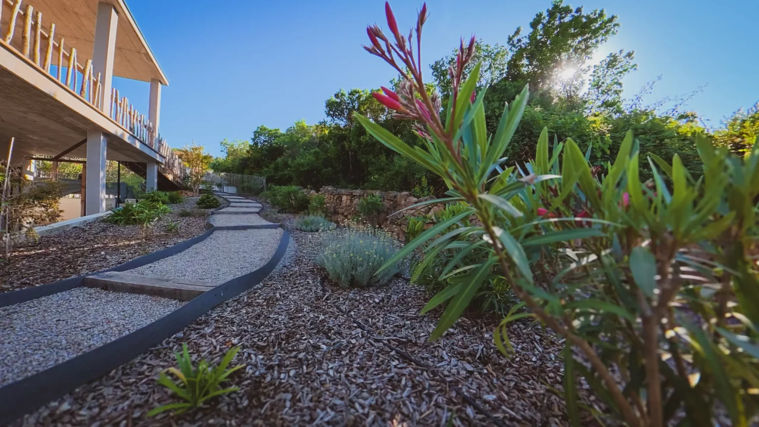 Allée de jardin paysager menant à une villa moderne en bois et pierre à Pietrosella en Corse du Sud.