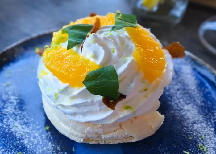 Dessert pavlova aux agrumes et chantilly maison sur assiette artisanale bleue du restaurant Tempi Fa
